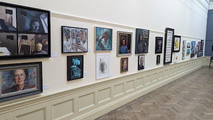 Artwork displayed on a gallery wall with a long wooden panel, and a wooden floor.