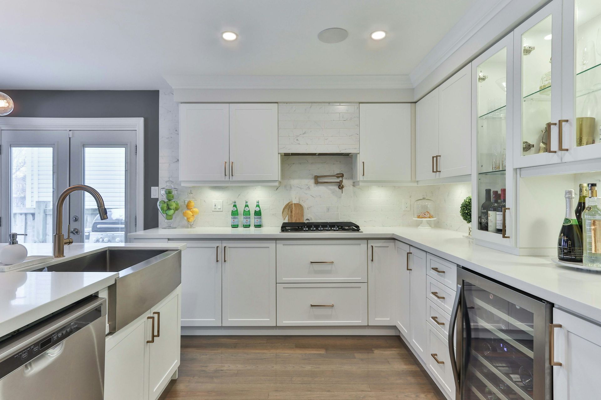 Modern white kitchen with stainless steel appliances, a wine fridge, and wooden floor.