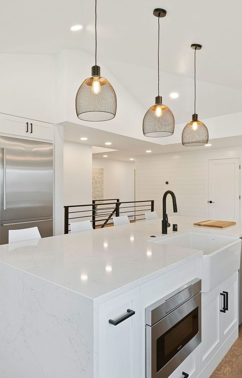 Modern white kitchen with island, pendant lights, black faucet, and microwave.