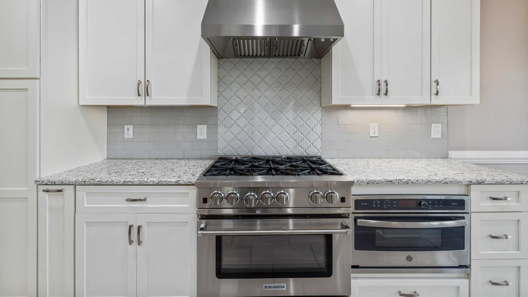 Stainless steel range and oven in a white kitchen with granite countertops and white cabinets.