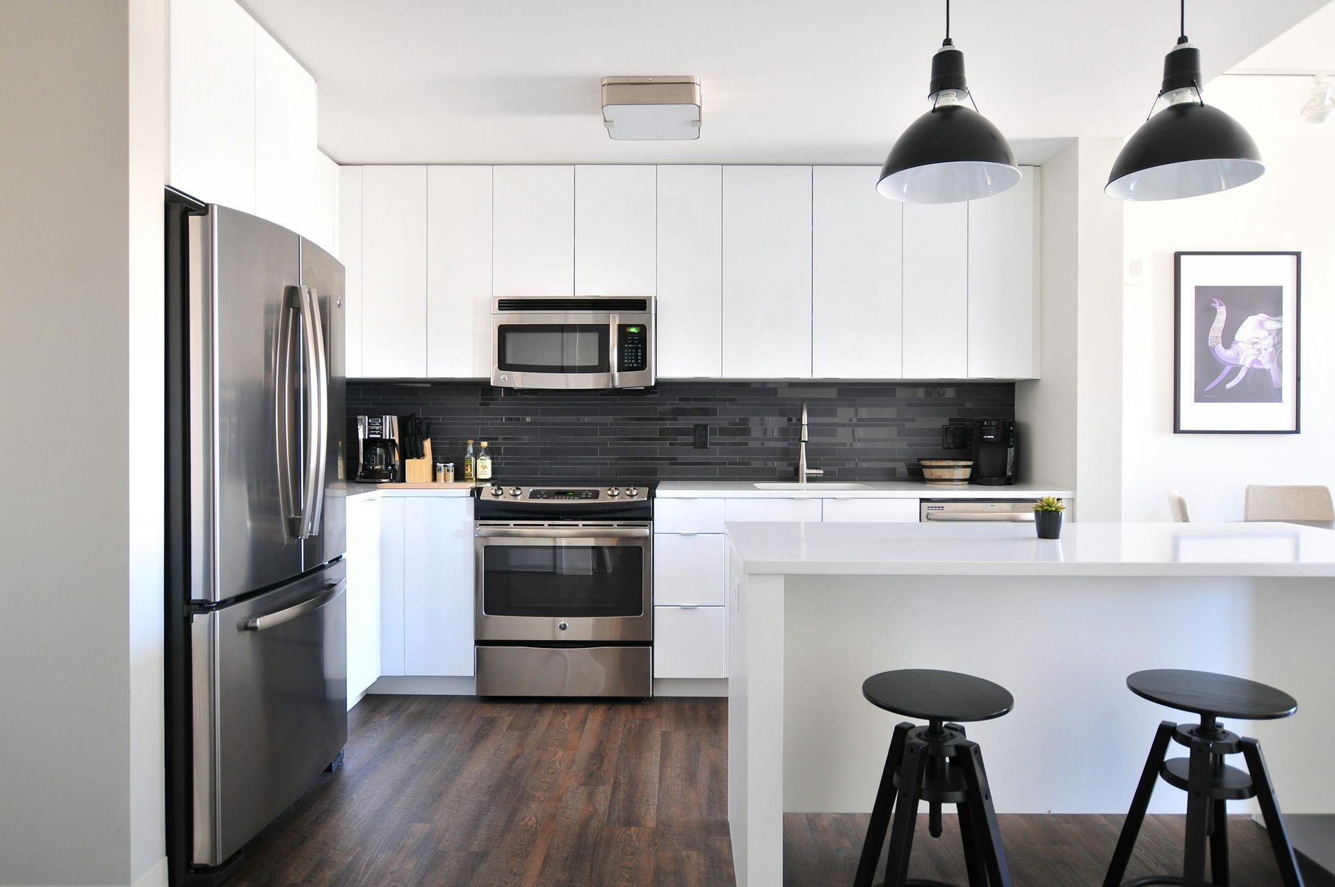 Modern white kitchen with stainless steel appliances, black backsplash, and dark wood floors.