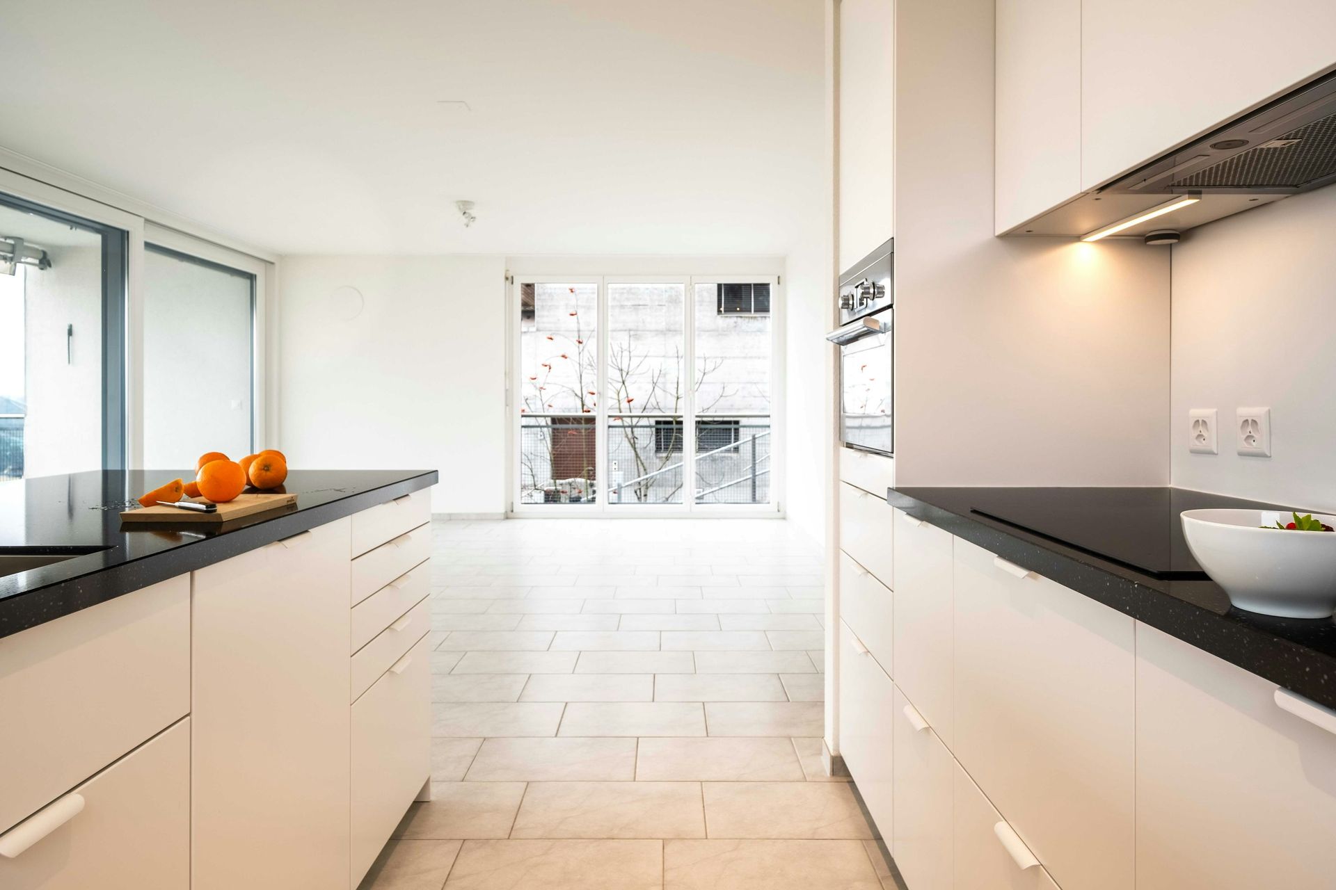 Modern white kitchen with black countertops, island, and large windows.