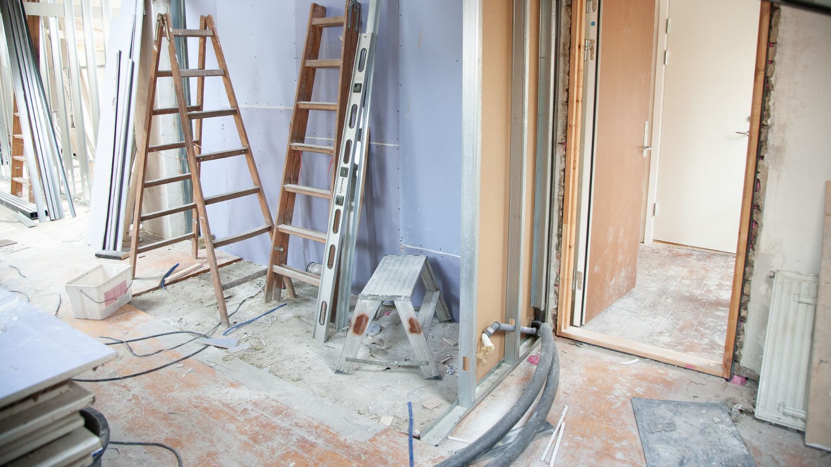 Room under renovation; two wooden ladders, step stool, open doorway, exposed framing, and materials.