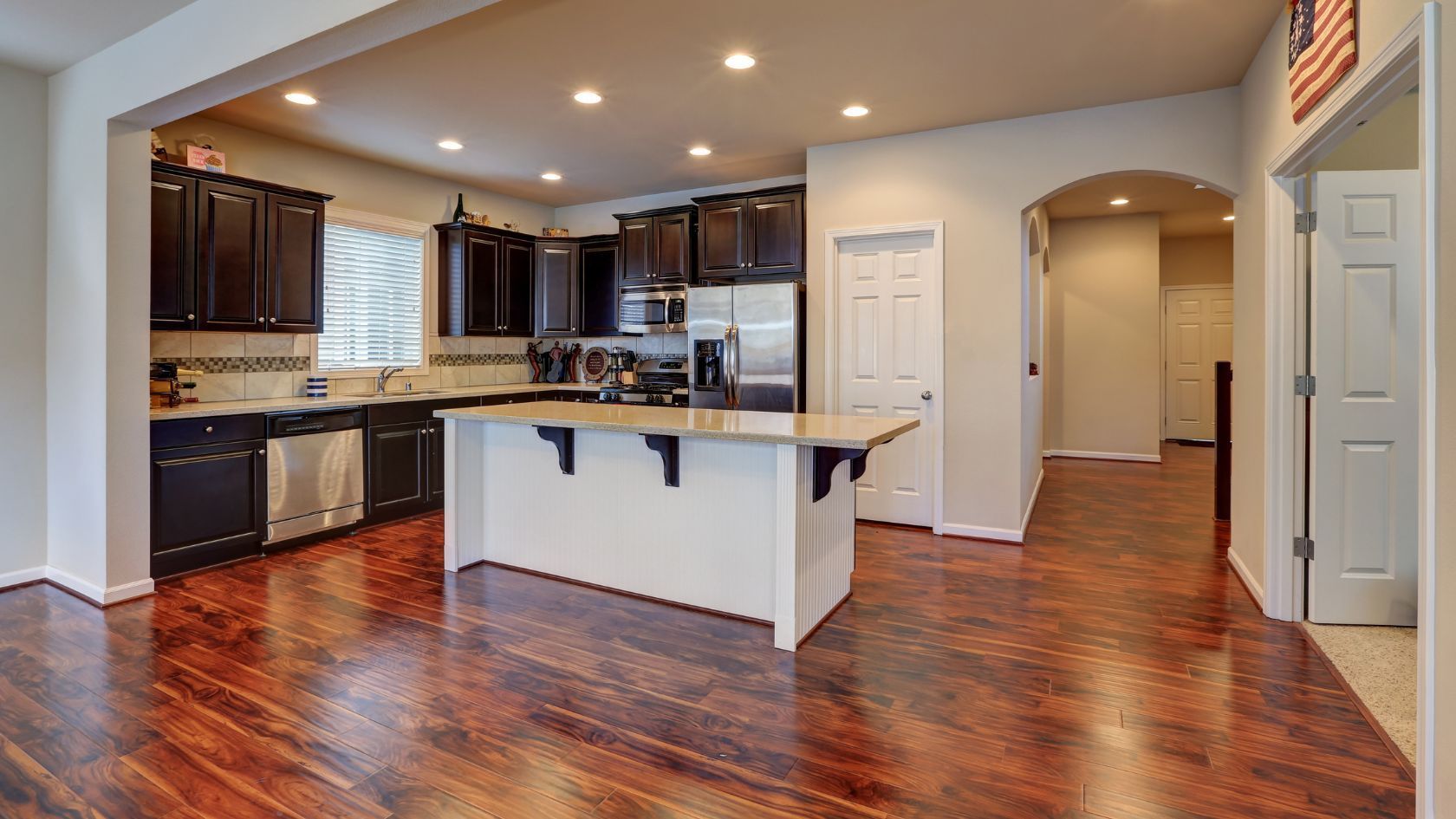 Kitchen with dark cabinets, stainless steel appliances, and a white island; hardwood floors.