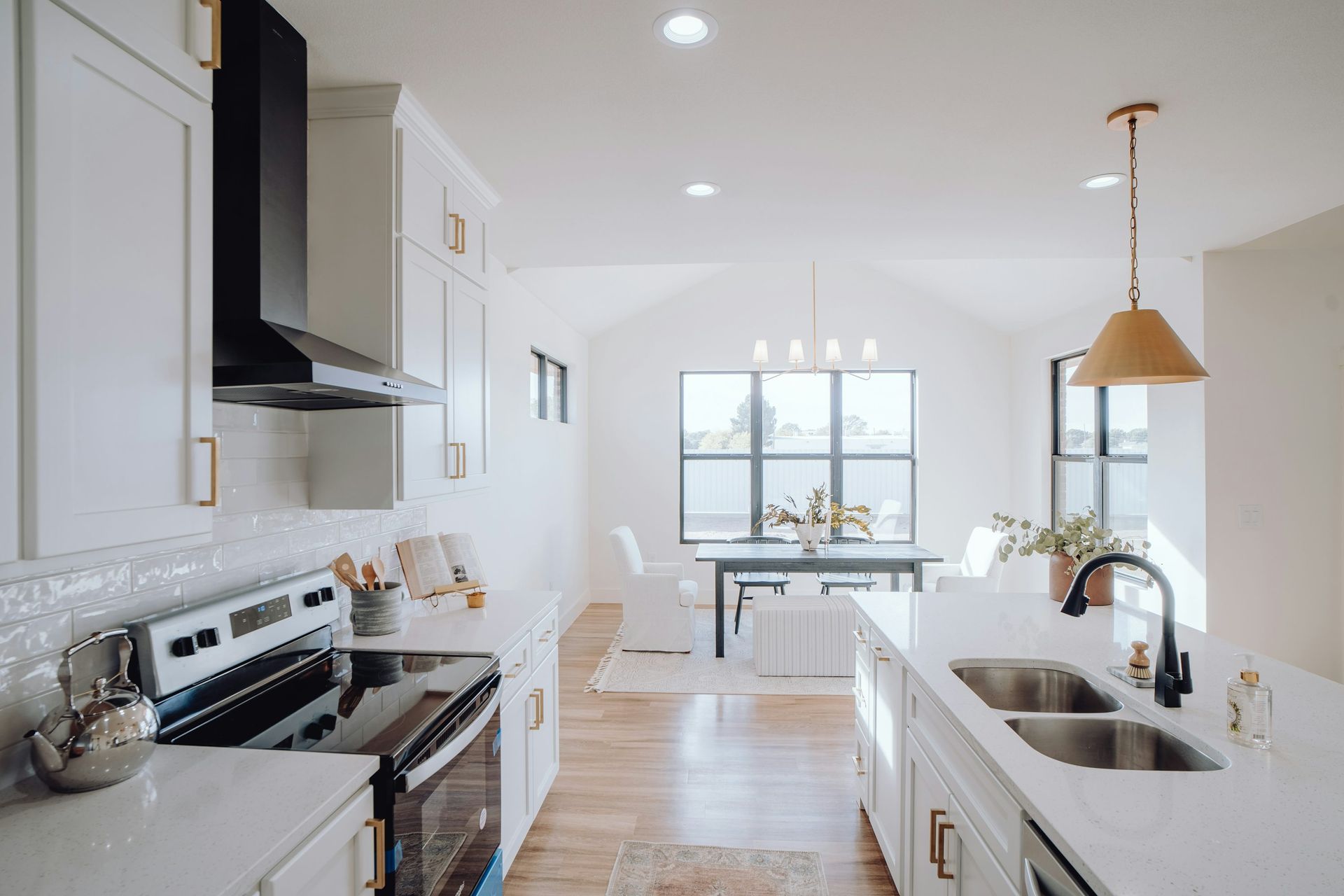 White modern kitchen with island, cabinets, and dining area with large window.