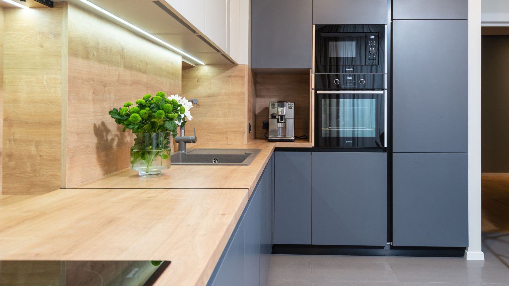 Modern kitchen with gray cabinets, light wood countertops, built-in oven, and a vase of flowers.