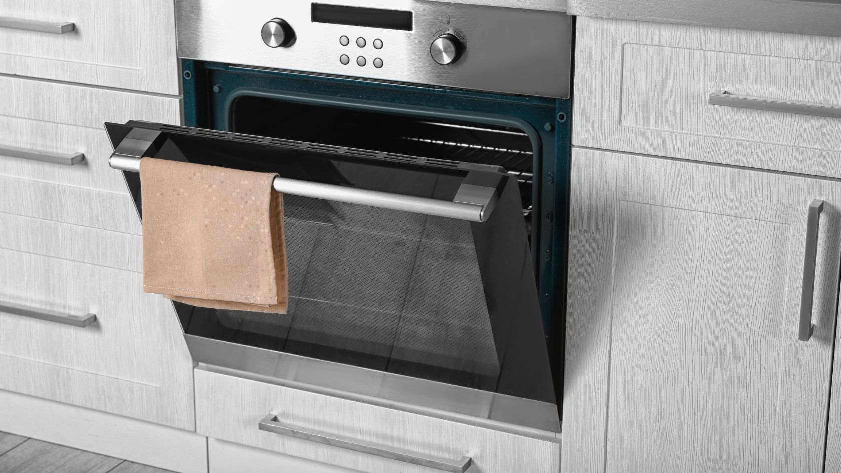 Oven with open door, brown paper bag hanging inside. White cabinets, stainless steel trim.