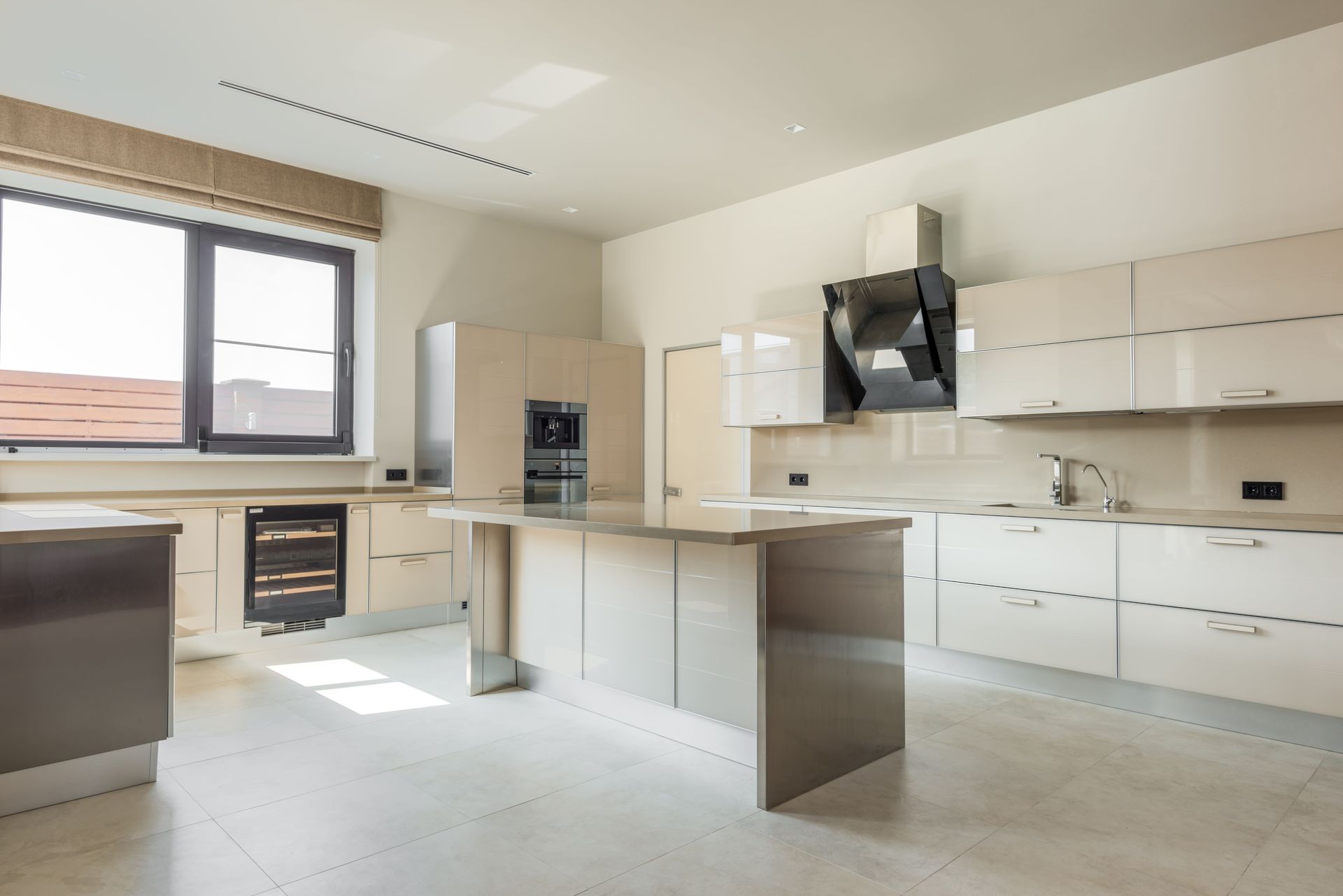 Bright modern kitchen with white cabinets, large window, island, and built-in oven.