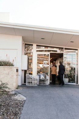 People entering a brightly lit shop with glass doors; white building, neutral colors.