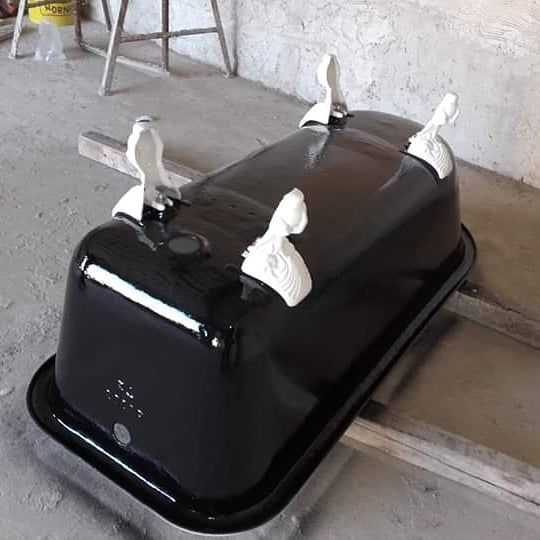 Bañera de color negro con patas de garra de color blanco, apoyada sobre soportes de madera.