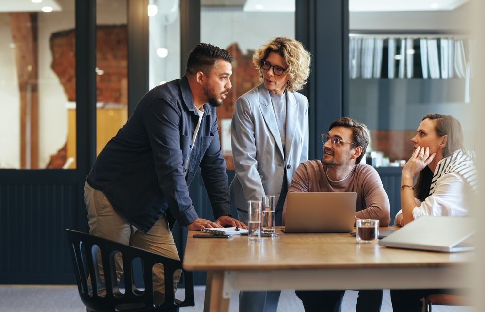 A group of people are sitting around a table looking at a laptop.