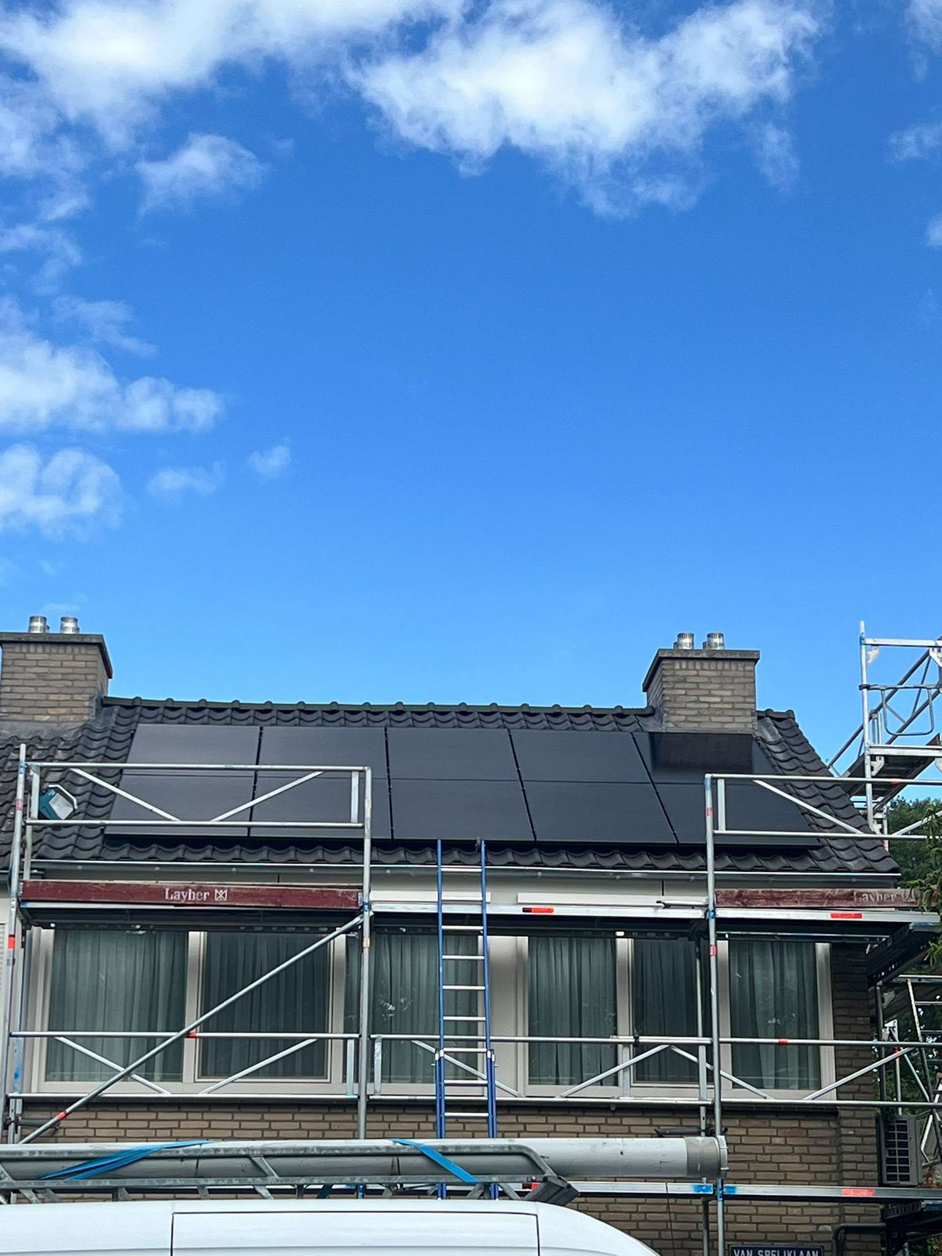 Een huis met zonnepanelen op het dak en een busje ervoor geparkeerd.