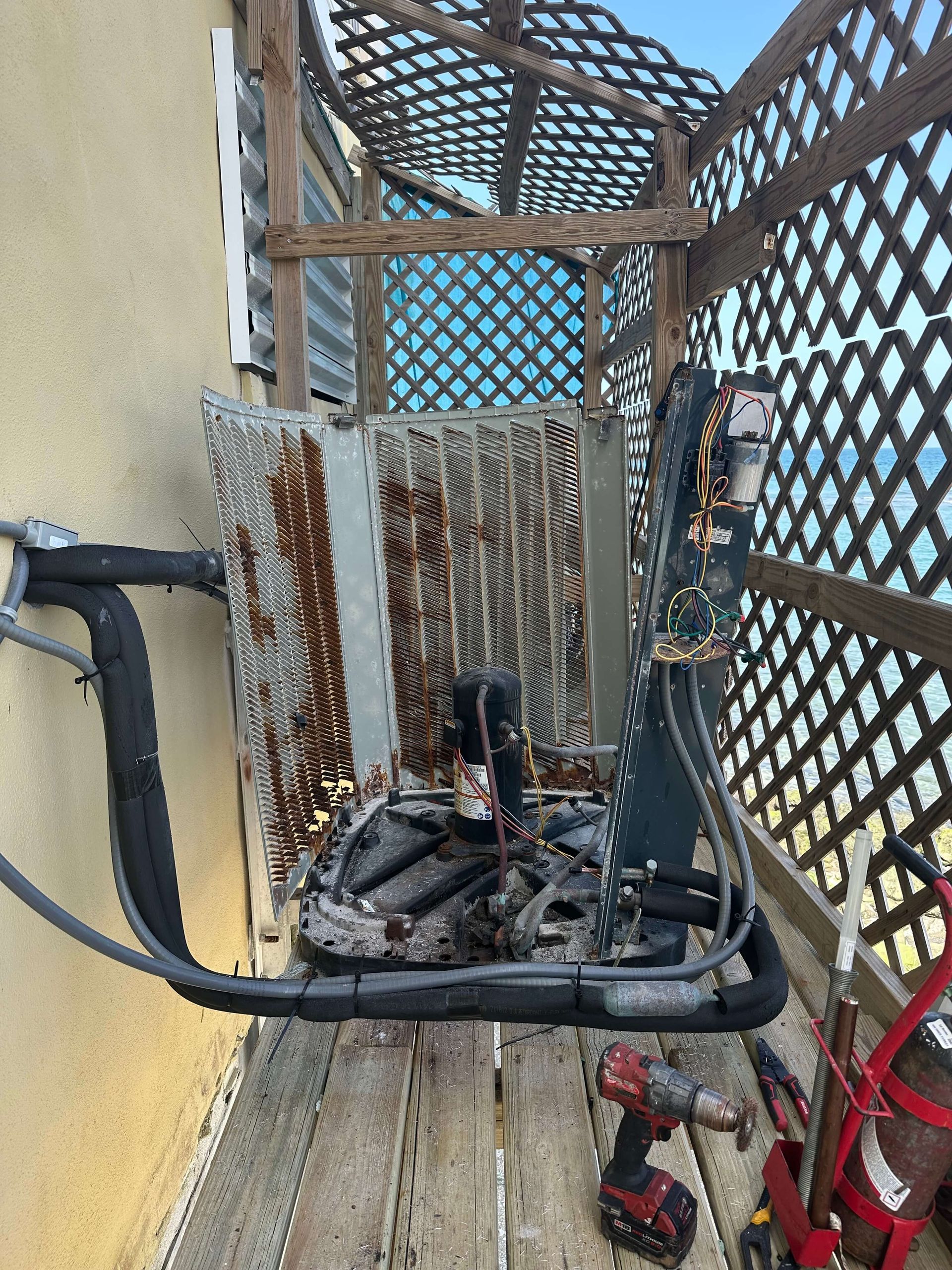 A broken air conditioner is sitting on a wooden deck next to a building.