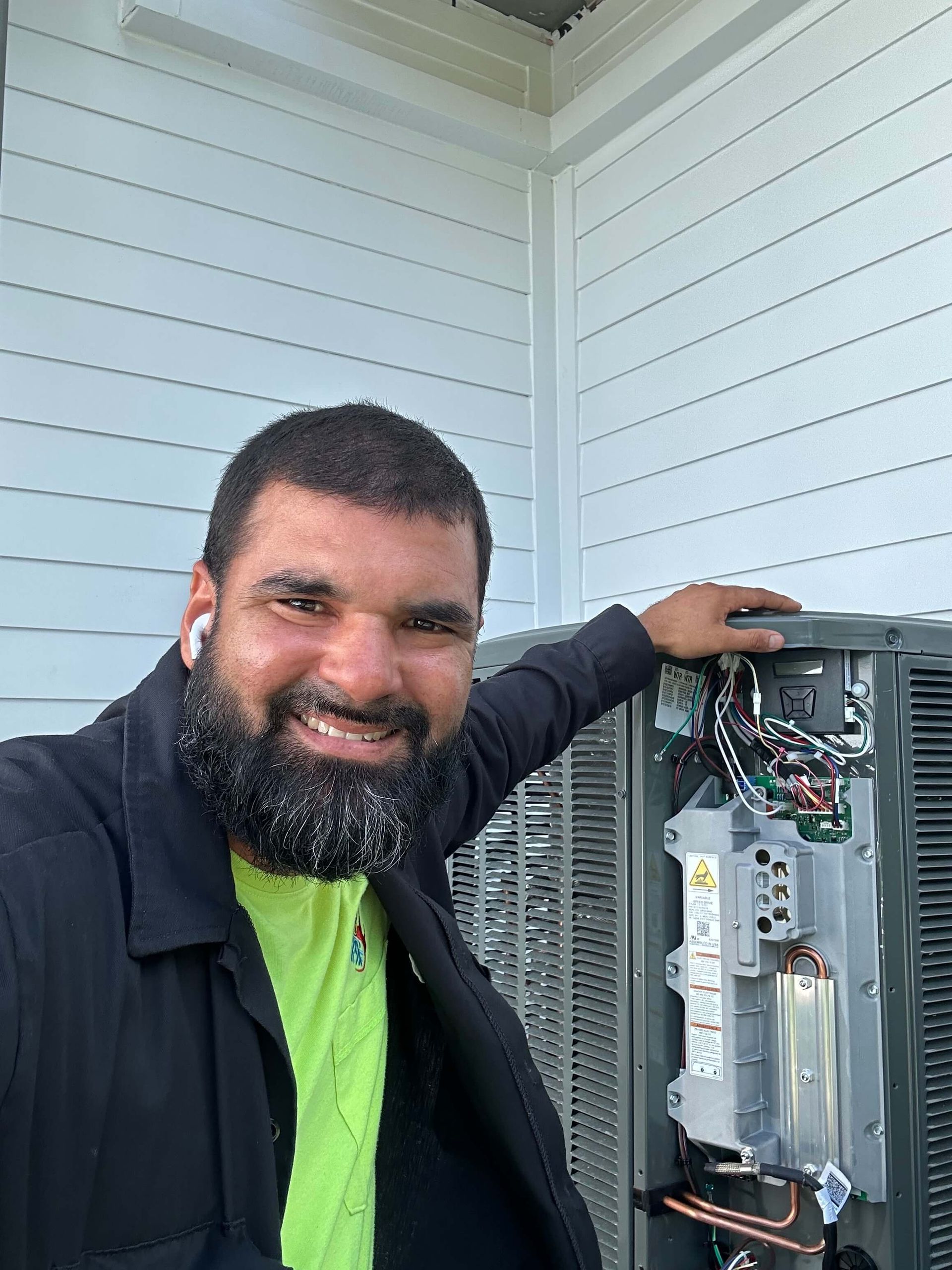A man with a beard is standing next to an air conditioner.