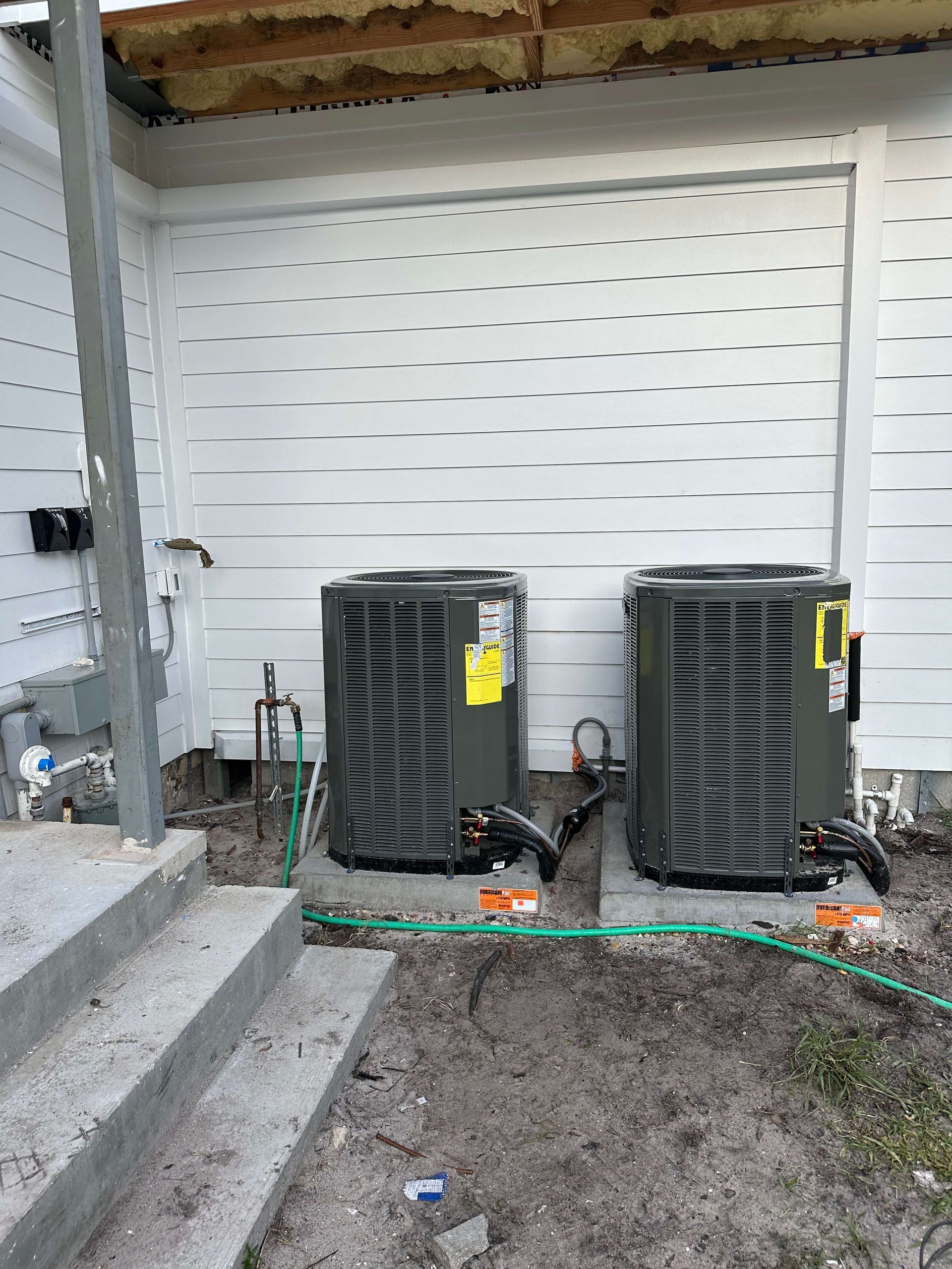 Two air conditioners are sitting next to each other on the side of a building.