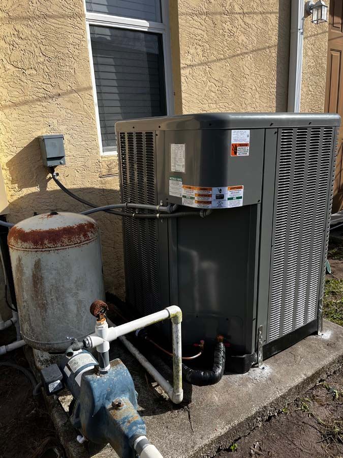 An air conditioner is sitting on the side of a building next to a water pump.