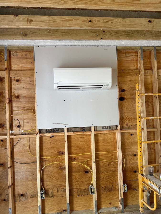 A wall mounted air conditioner is being installed in a room under construction.