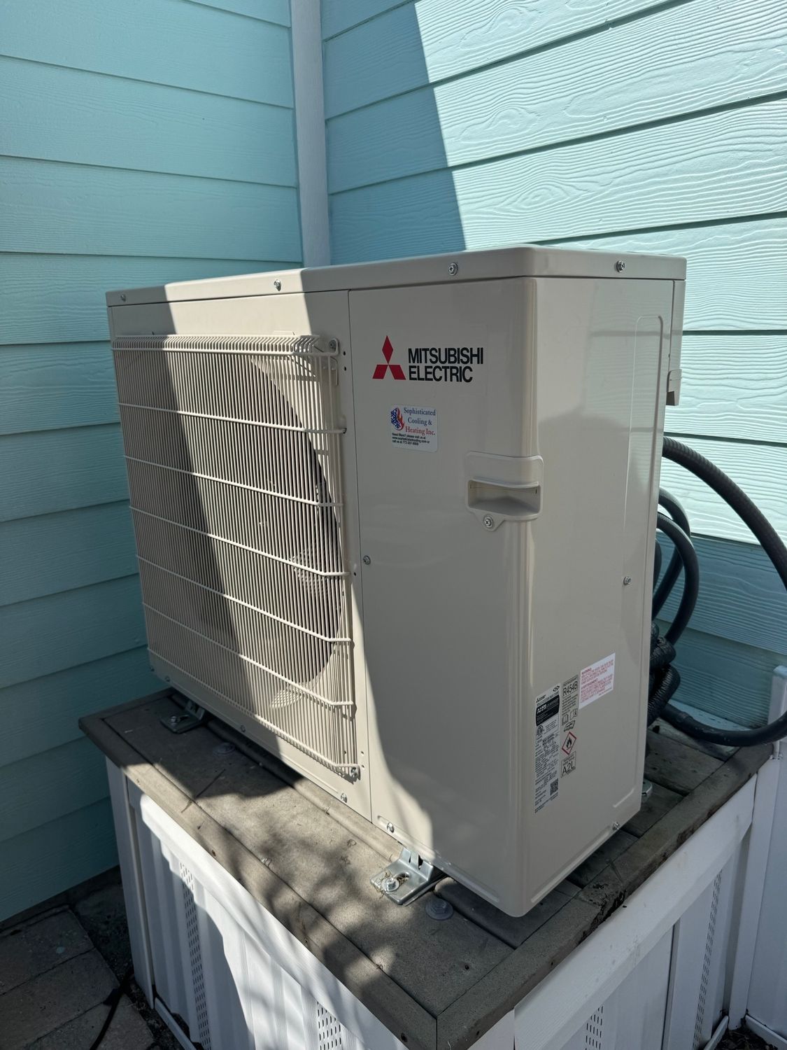 Mitsubishi Electric air conditioning unit, beige, mounted on a white base, next to a blue wall.