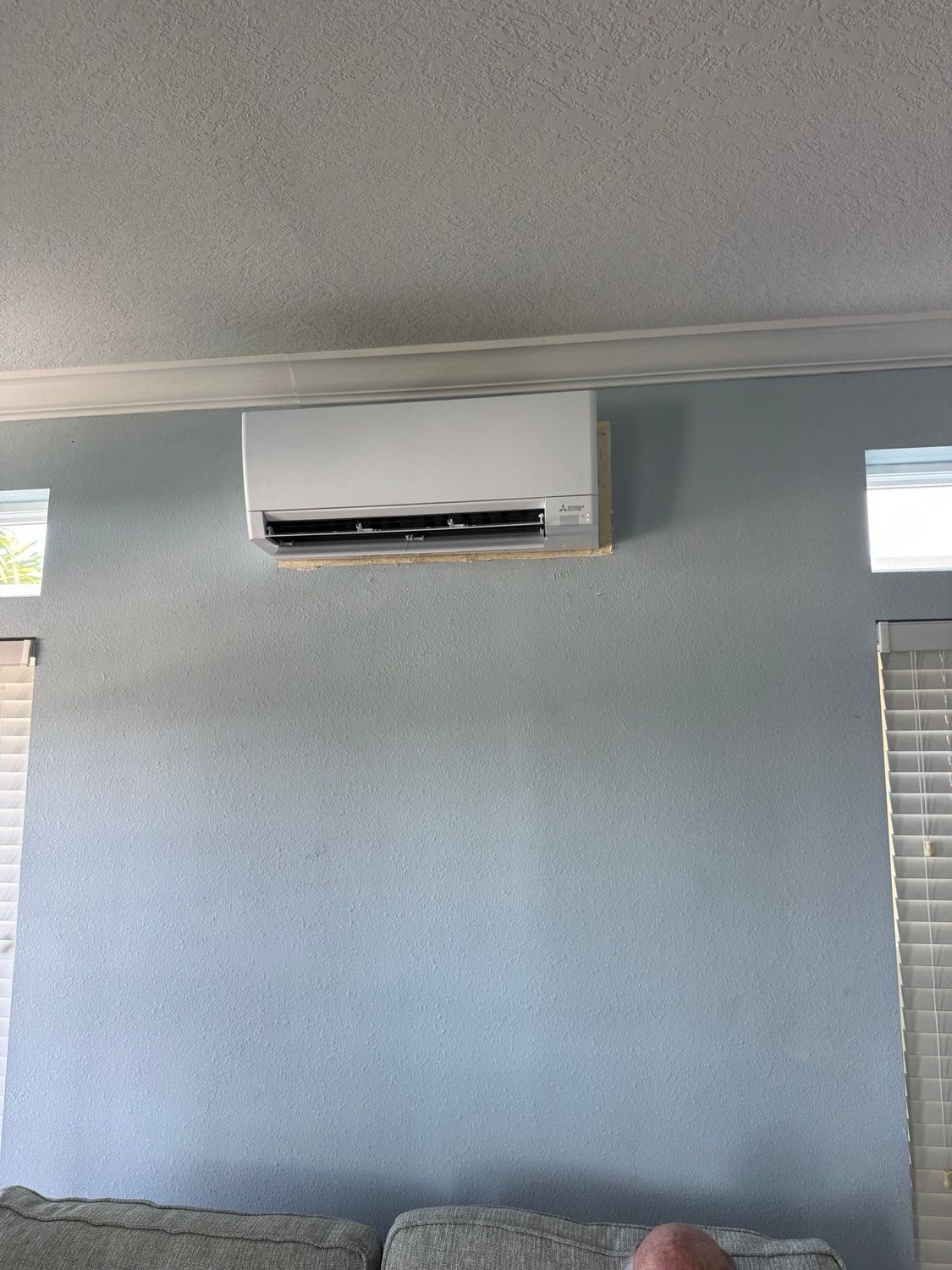 Blue wall with a white wall-mounted air conditioner, windows on each side.