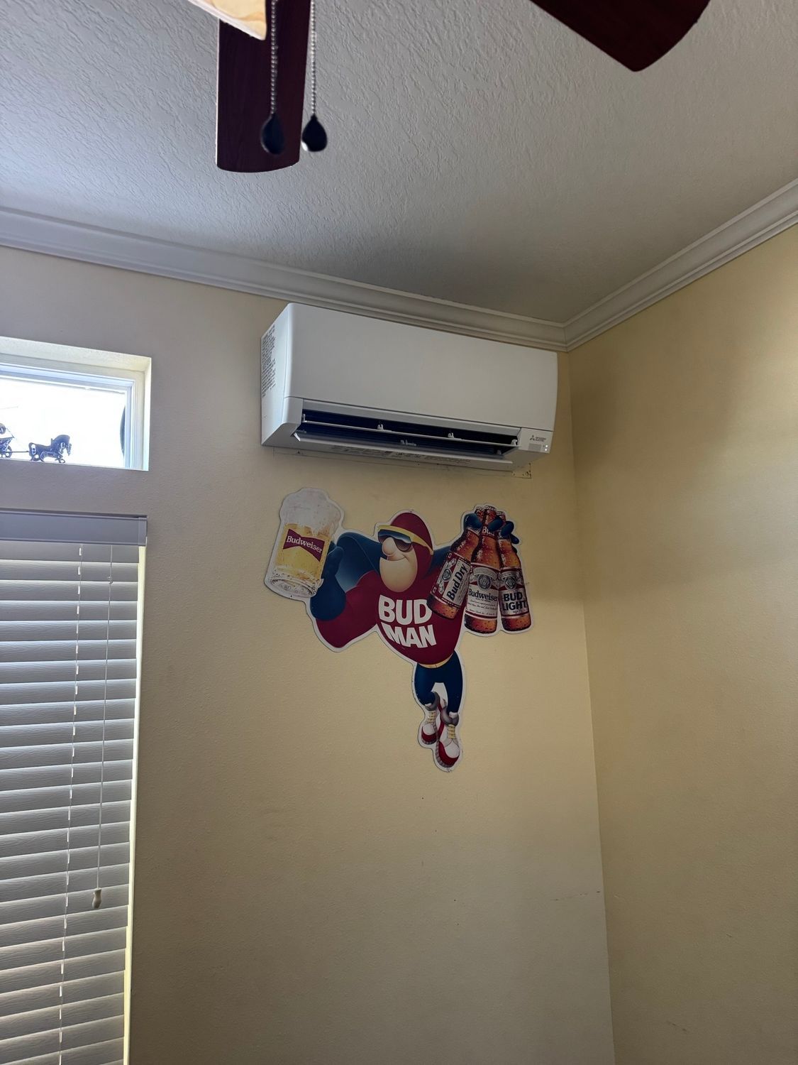 Air conditioning unit above a Bud Man sticker on a cream-colored wall.