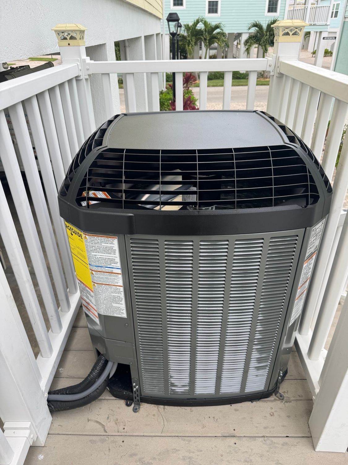 Air conditioning unit enclosed by a white railing on a porch.