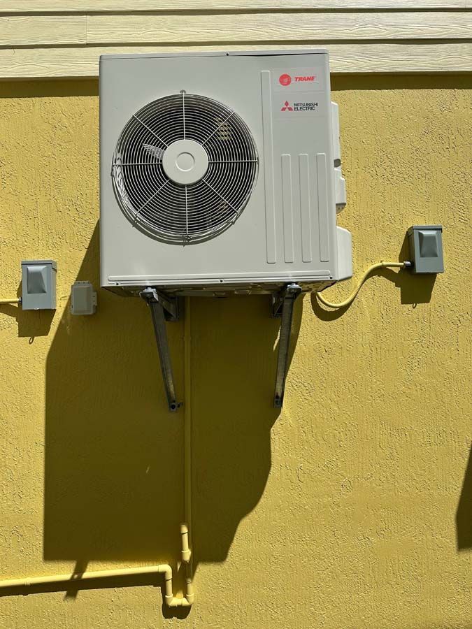 A white air conditioner is mounted on a yellow wall.