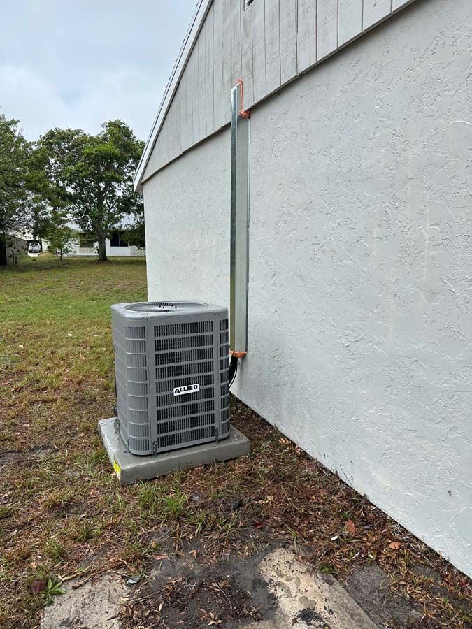 A gray air conditioner is sitting on the side of a white building.