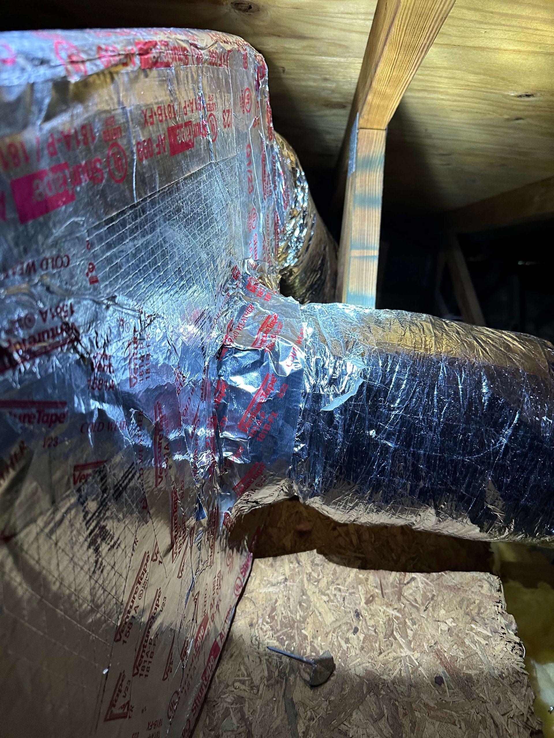 A piece of aluminum foil is wrapped around a pipe in an attic.