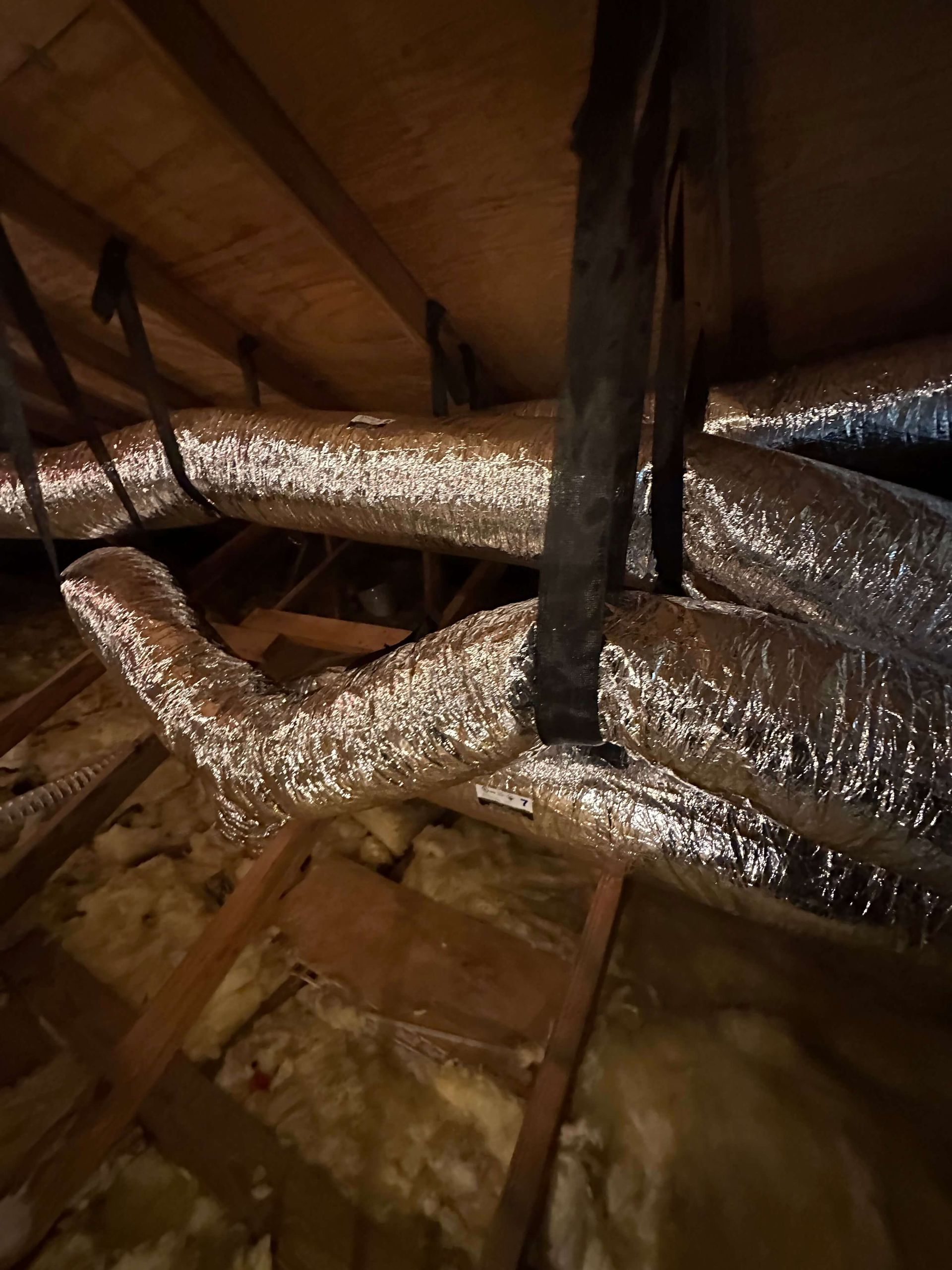 A bunch of ducts are hanging from the ceiling of an attic.
