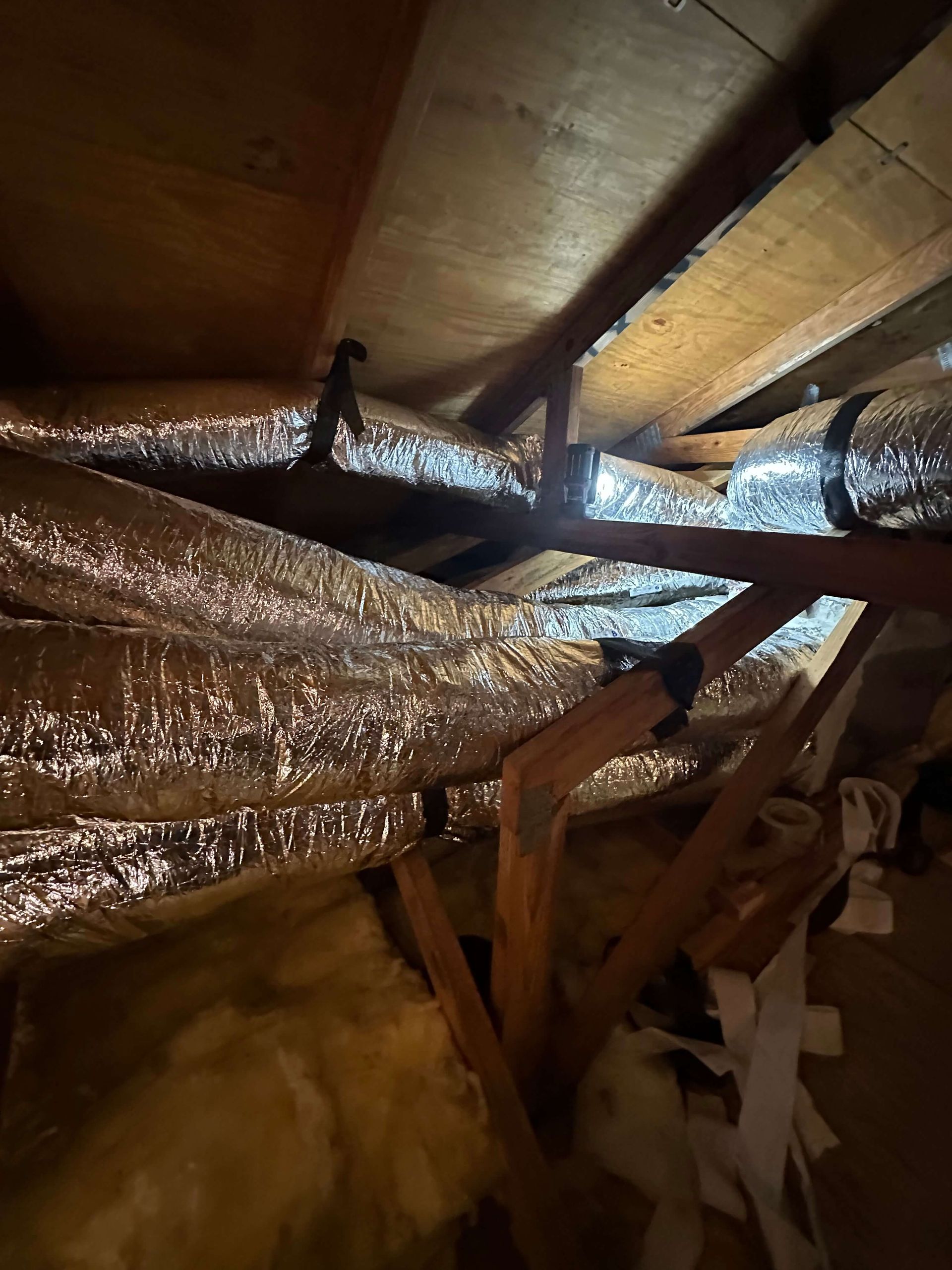 A bunch of ducts are hanging from the ceiling of an attic.