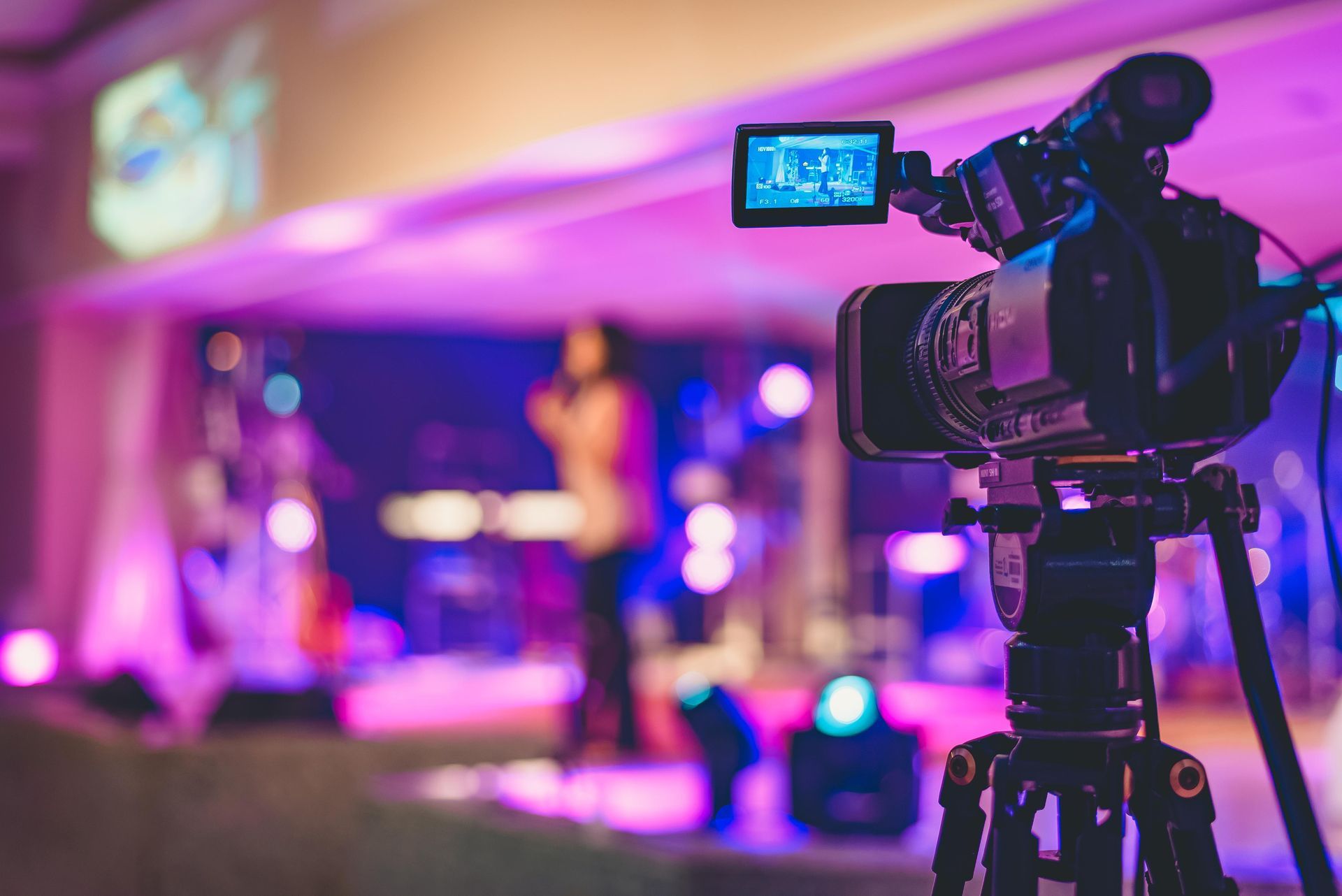 A camera on a tripod filming a brightly lit stage with a person performing.