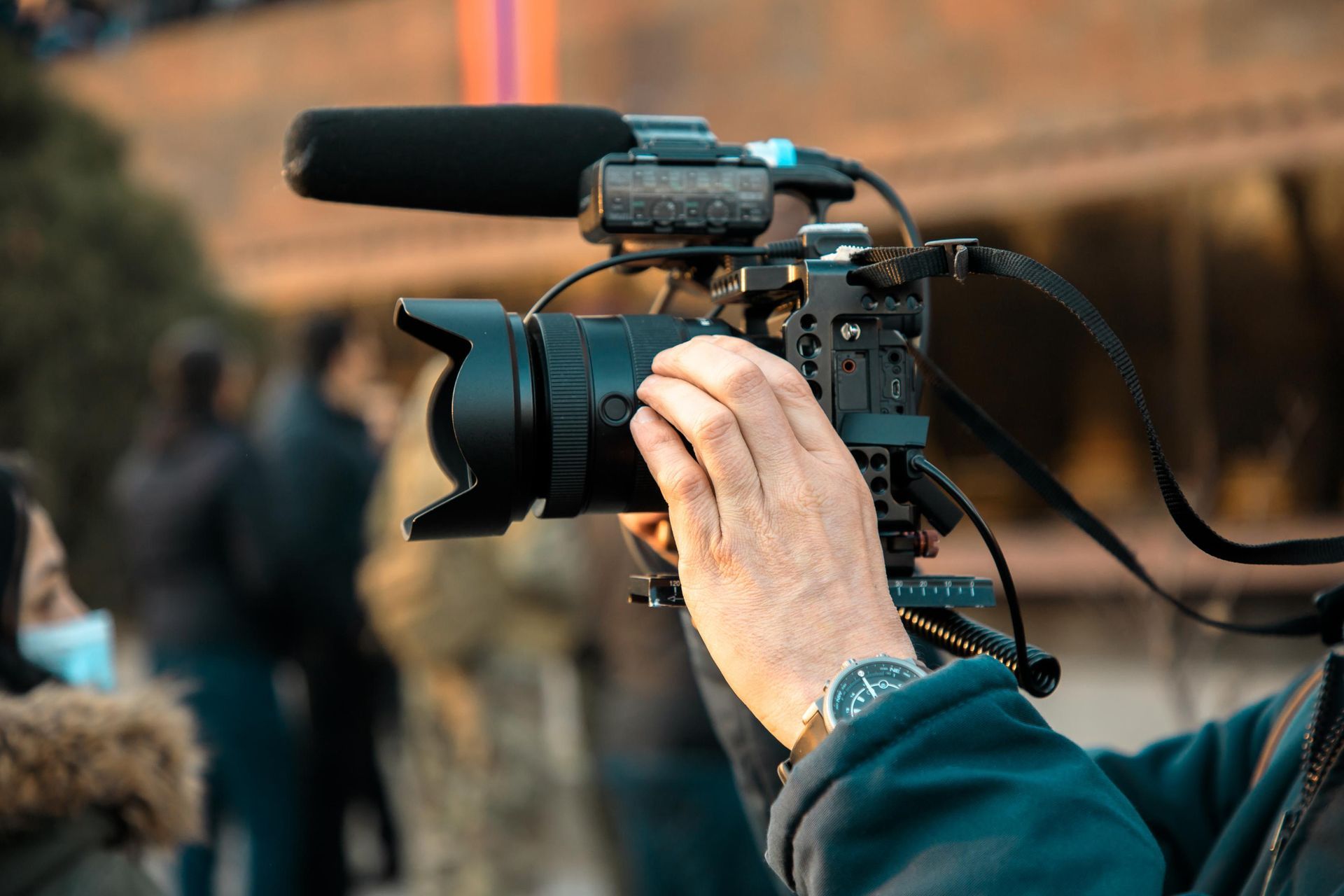 A person holding a video camera with a microphone attached, filming outdoors.