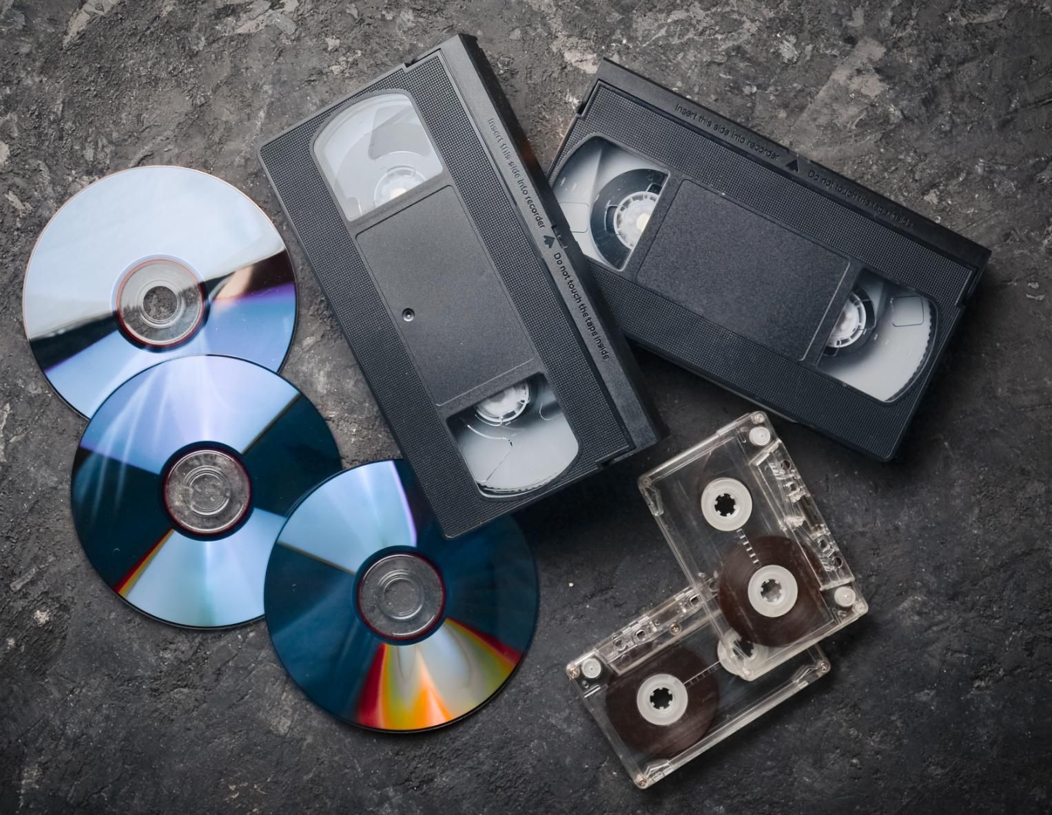 CDs, VHS tapes, and cassette tapes on a textured gray surface.