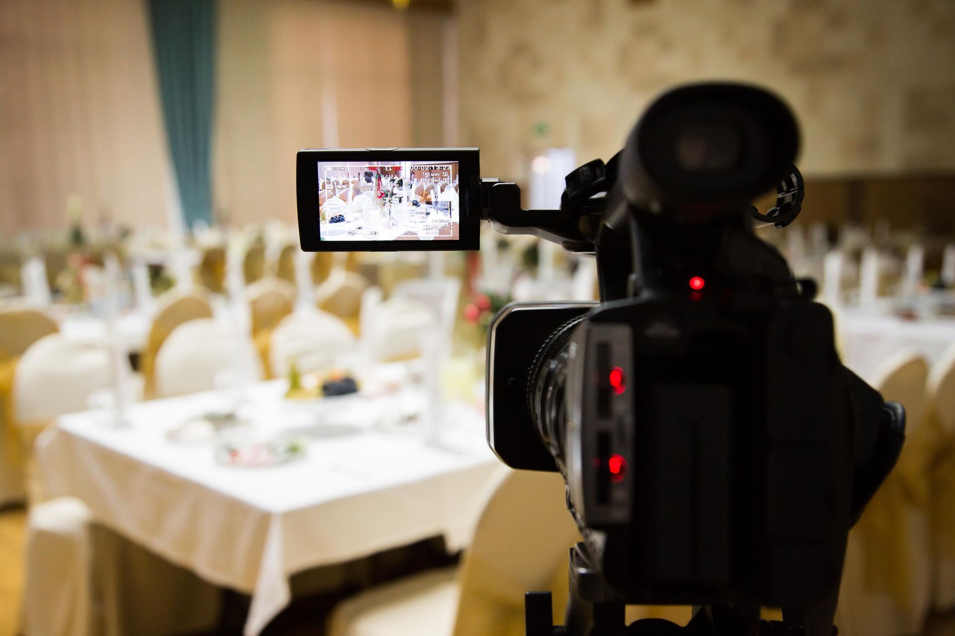 Video camera filming a banquet hall with tables set for an event.