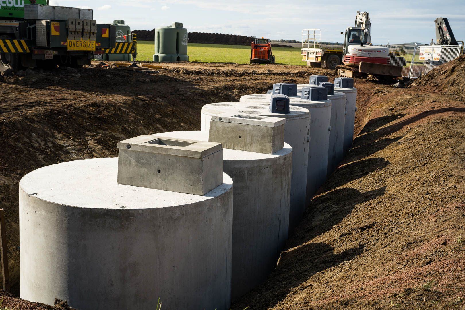 A series of cylindrical concrete utility structures partially buried in a dirt construction trench.