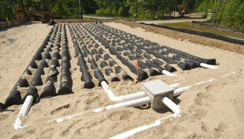 A leach field for a septic system with rows of black plastic drain covers resting on sand, connected to a central junction.