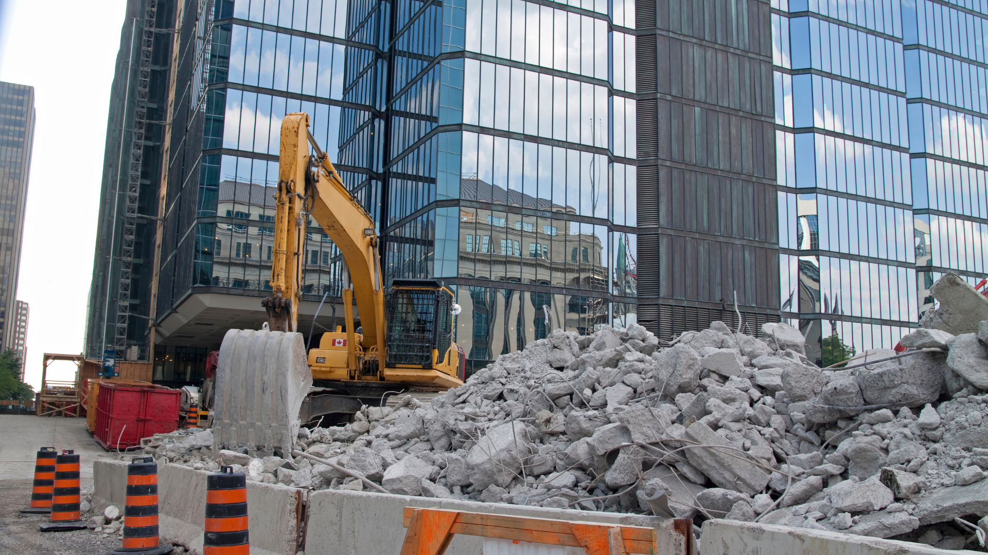 A construction site with a large building in the background and a pile of concrete in the foreground.
