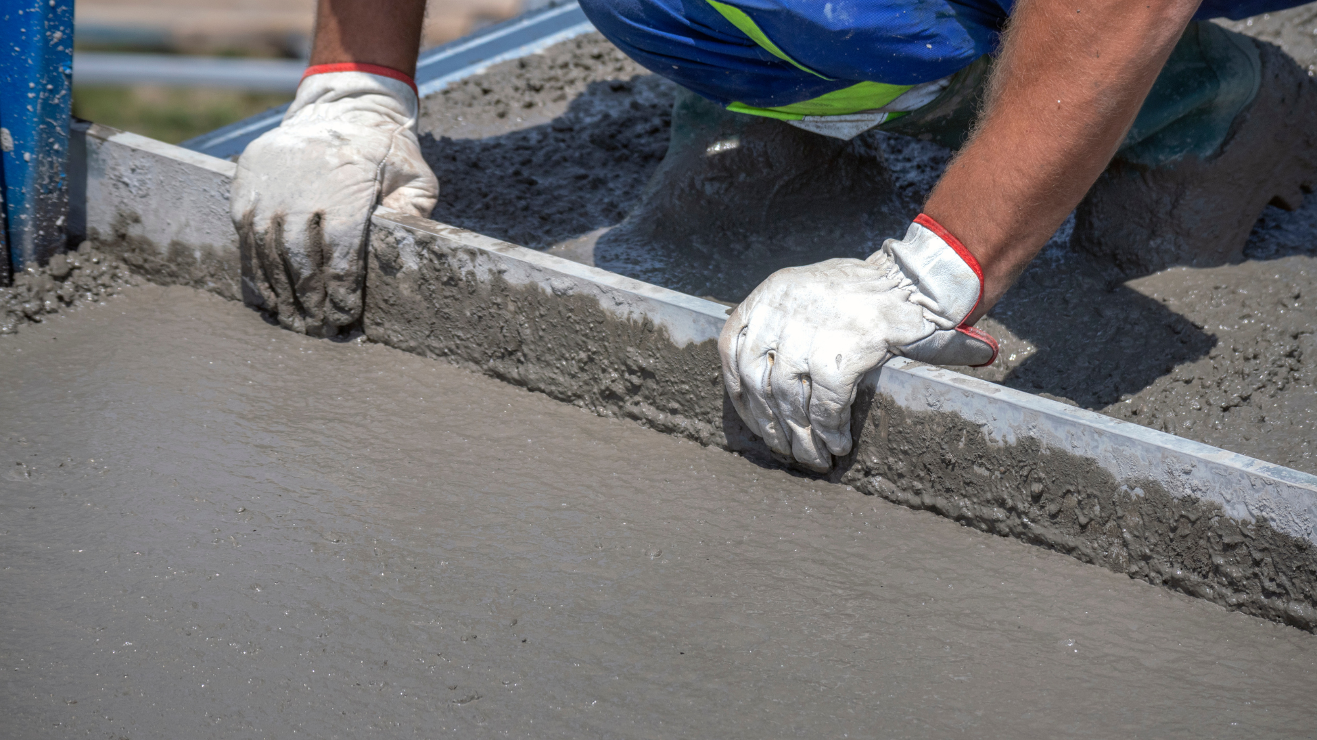 A man is laying concrete on the ground with a ruler.