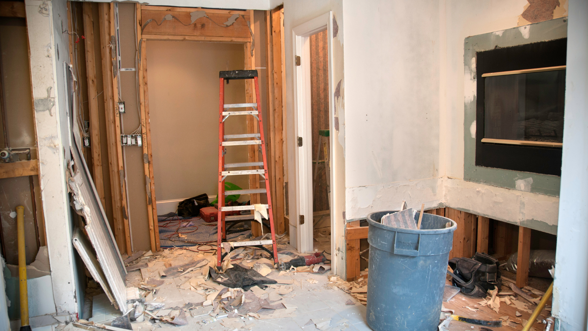 A living room under construction with a ladder and a trash can.