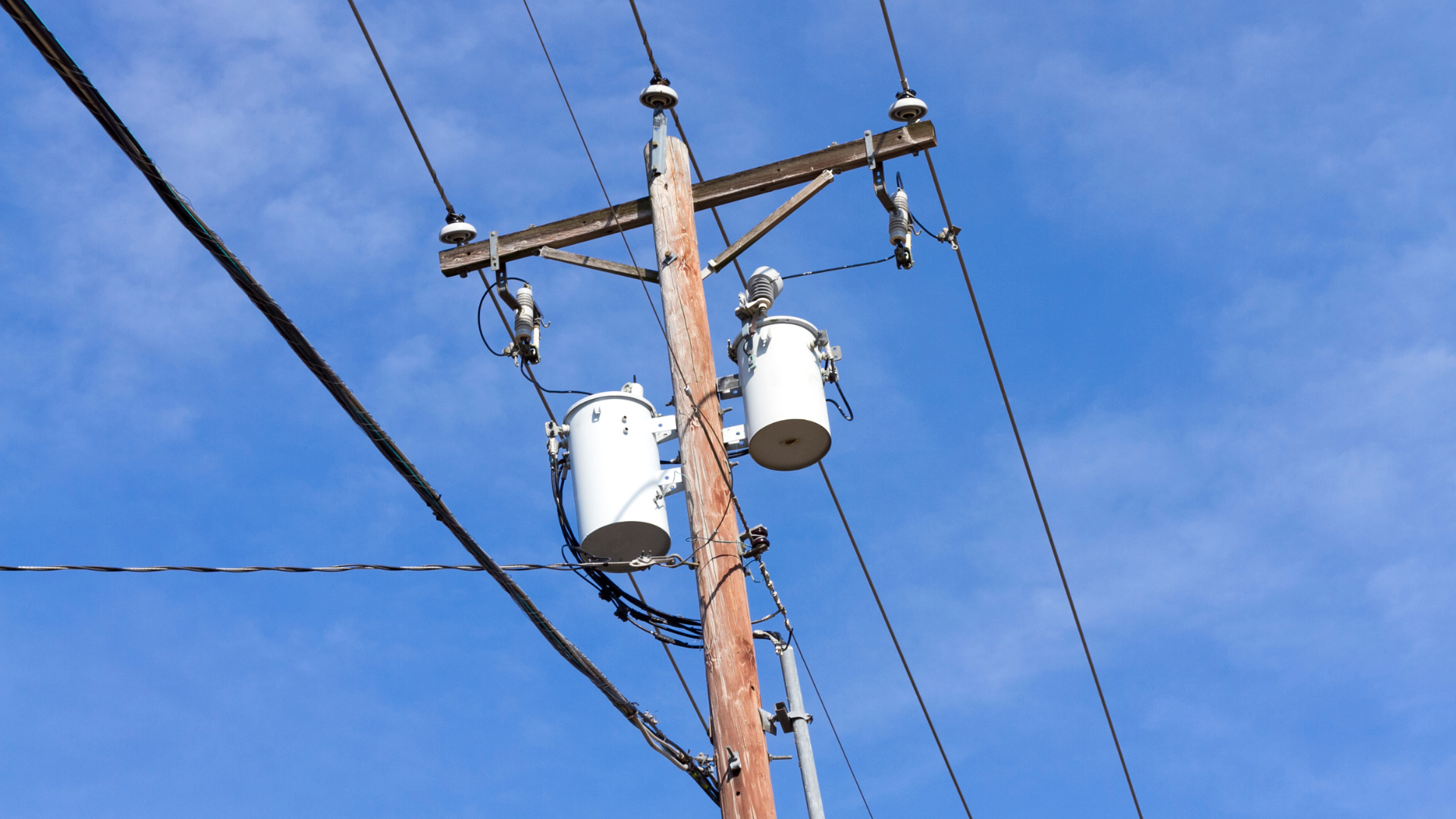 A power pole with two transformers attached to it against a blue sky.