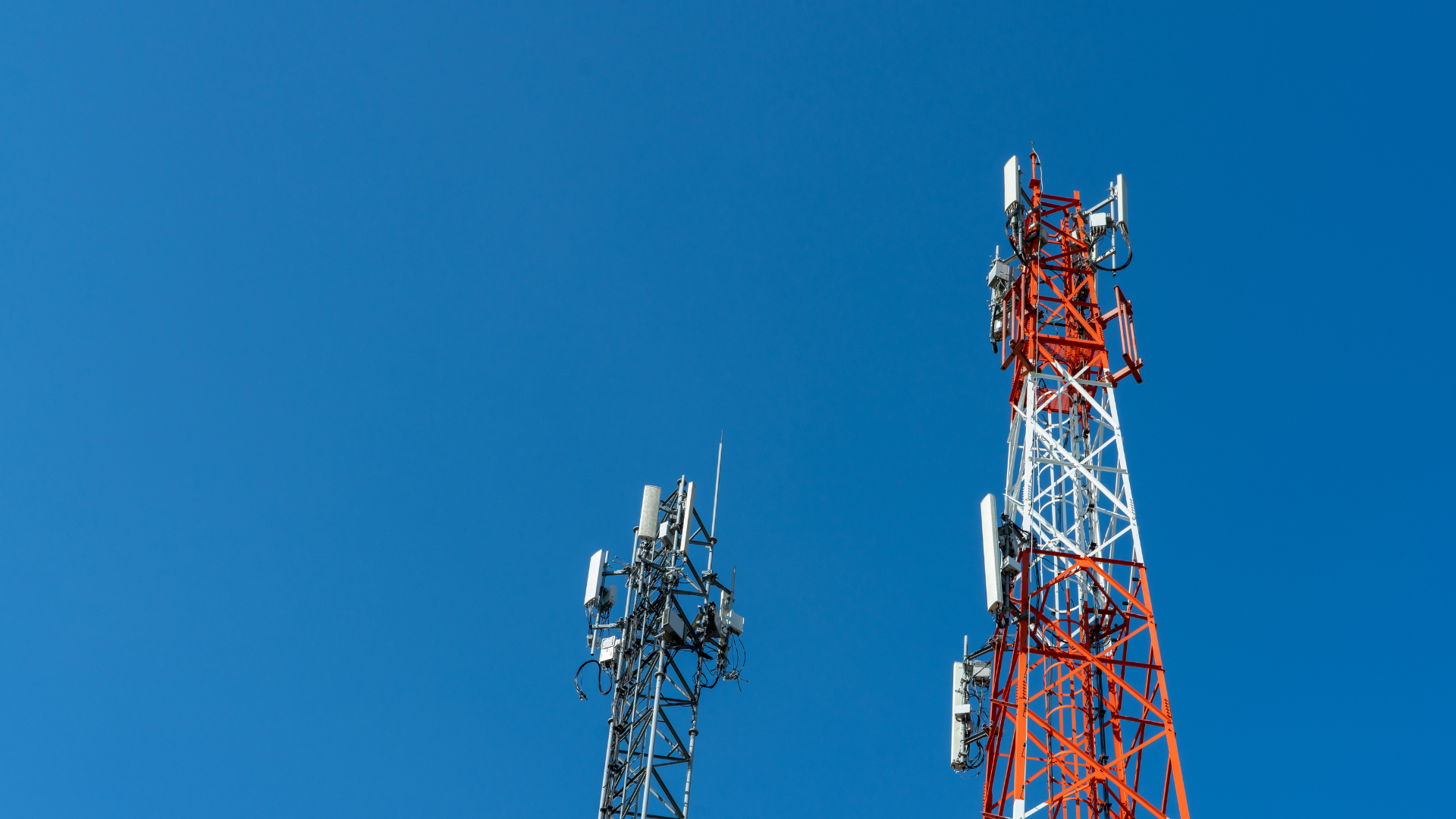 Two telephone towers are against a blue sky.