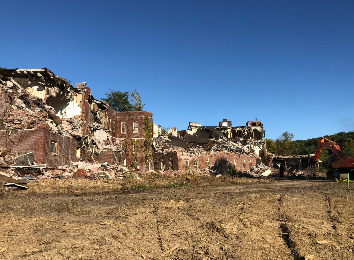 A large brick building is being demolished in a field.