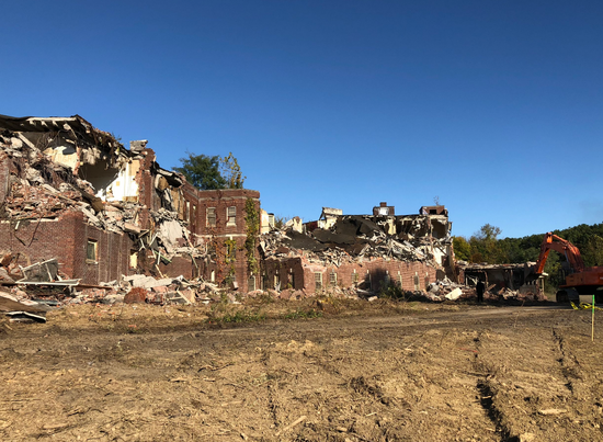 A large brick building is being demolished in a field.