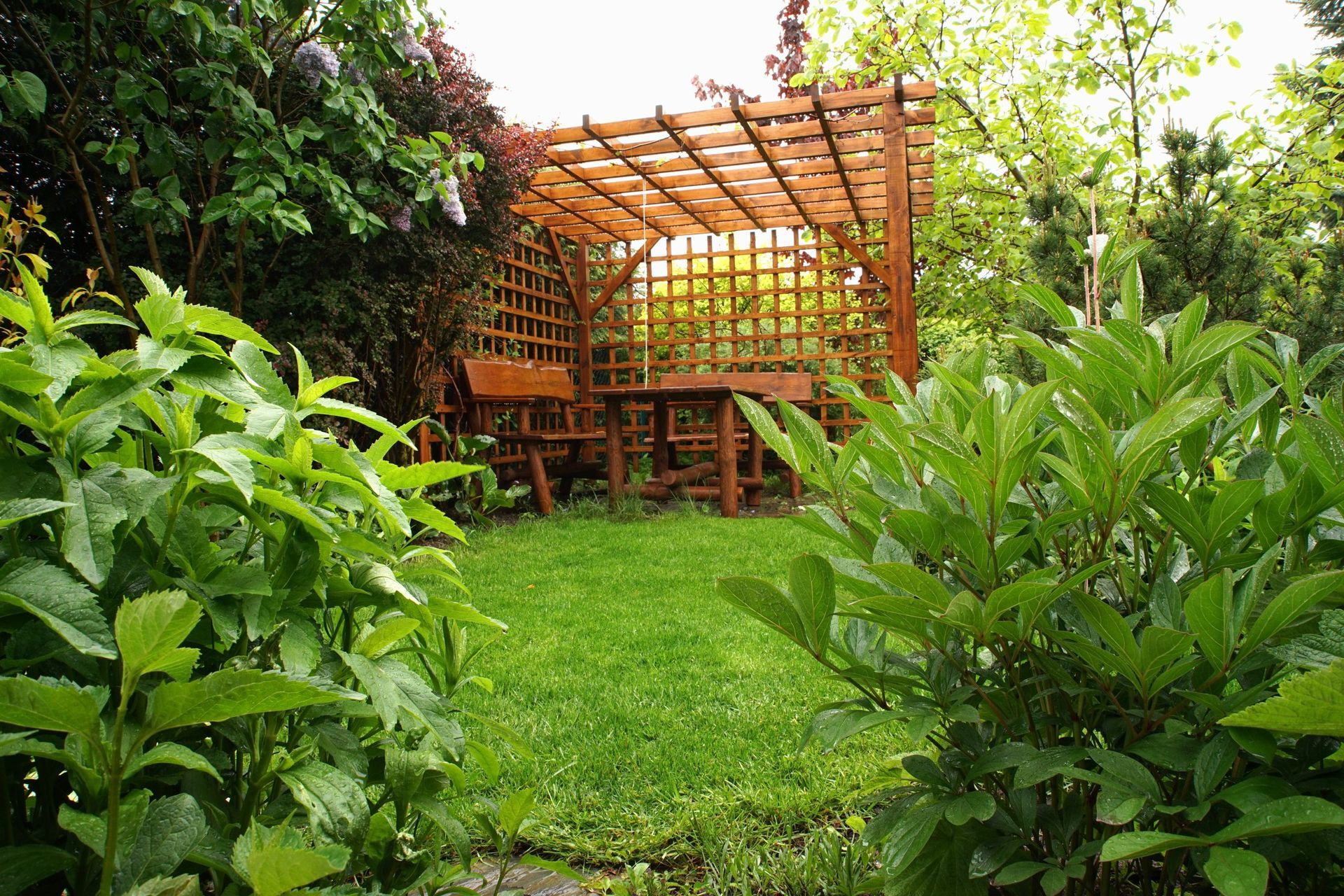 Wooden pergola with table and chairs in a lush green garden