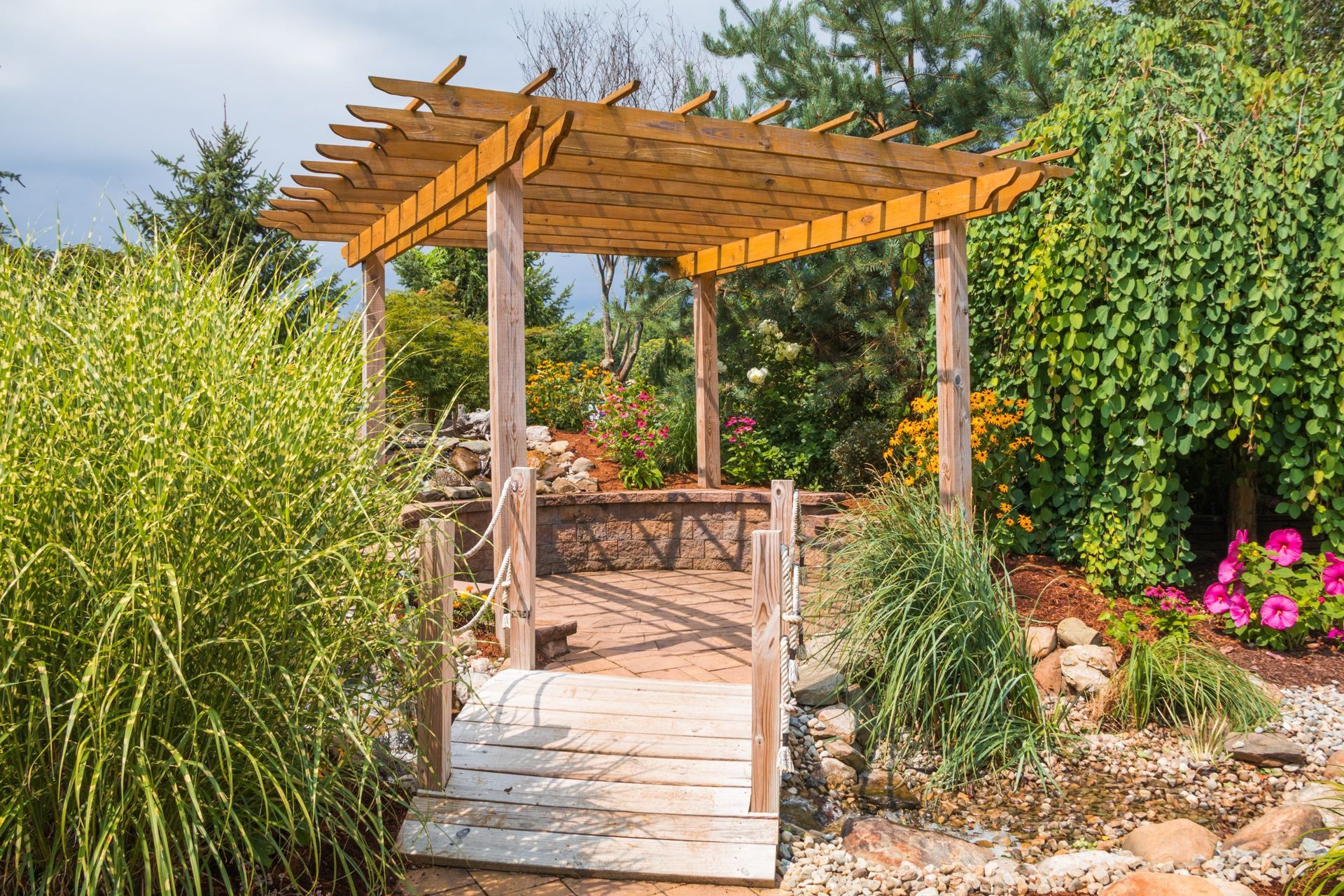 Wooden pergola with a bridge in a garden, surrounded by greenery and flowers
