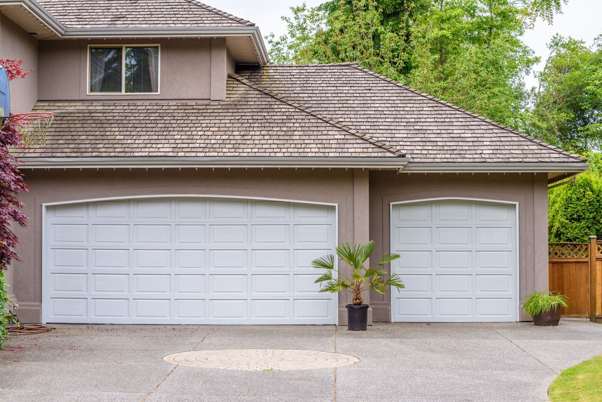 Two white garage doors on a light brown house with a stone driveway and a potted plant