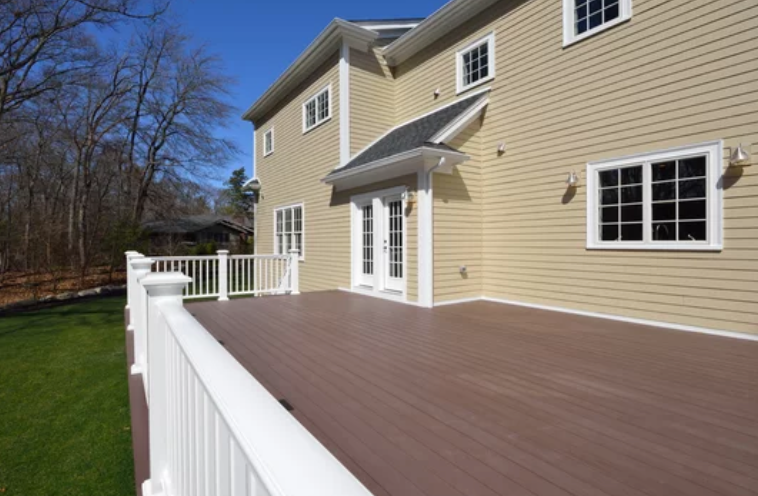 Large wooden deck with white railing on a two-story beige house with French doors and windows