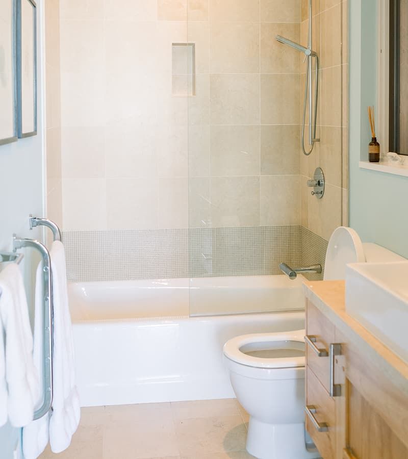Bathroom with a white tub, toilet, sink, light beige tile, and towel rack