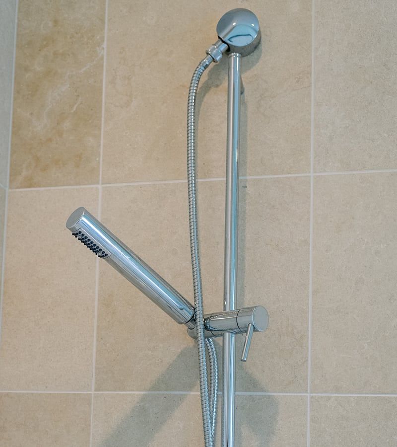Silver showerhead and hose on a vertical bar against beige tile