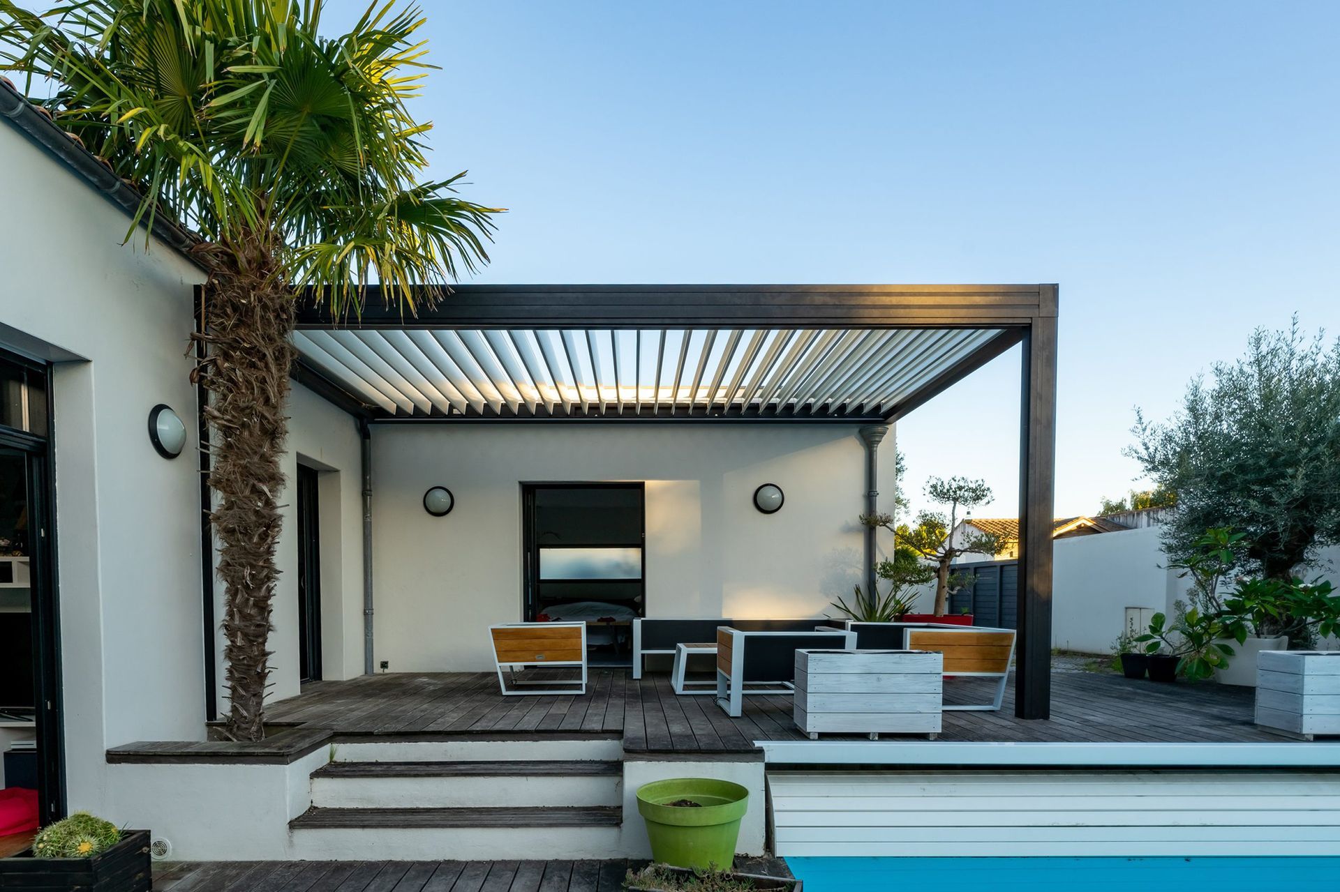 Pergola over outdoor seating area next to pool, white walls, dark wood